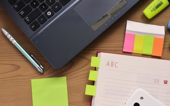 Top view of a workspace featuring a laptop, notebook, pen, and colorful stationery on a wooden desk.
