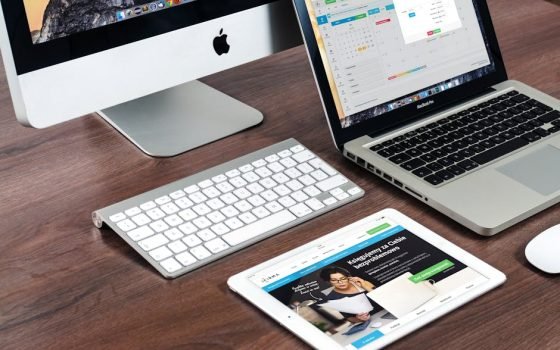 A sleek office desk setup featuring Apple devices: iMac, MacBook, and iPad.
